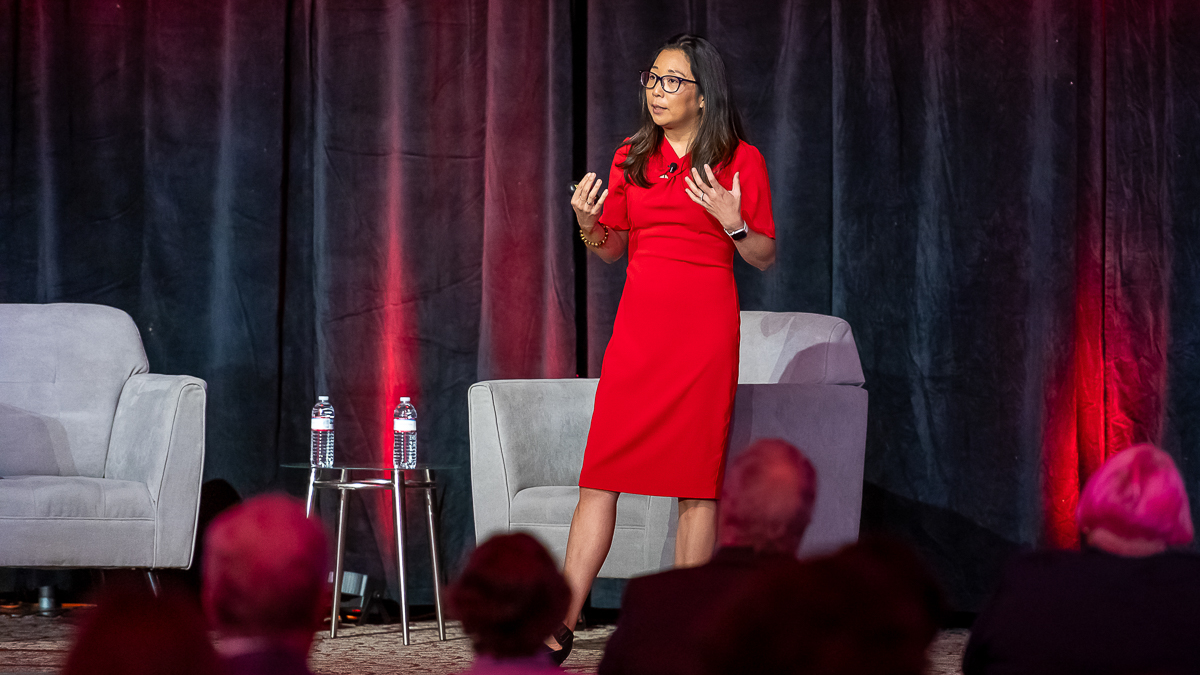 Woman in a red dress standing on stage speaking to an audience